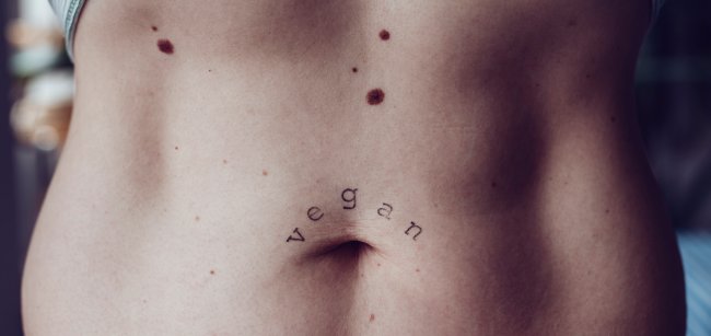 Entenda as principais diferenças entre o veganismo e o vegetarianismo Foto da barriga de uma mulher branca e magra; em cima do umbigo, tem uma tatuagem com o escrito: vegan