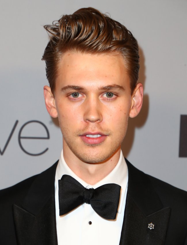 Austin Butler posando para foto em carpet com expressão neutra; ele usa terno e gravata borboleta preta com camisa branca