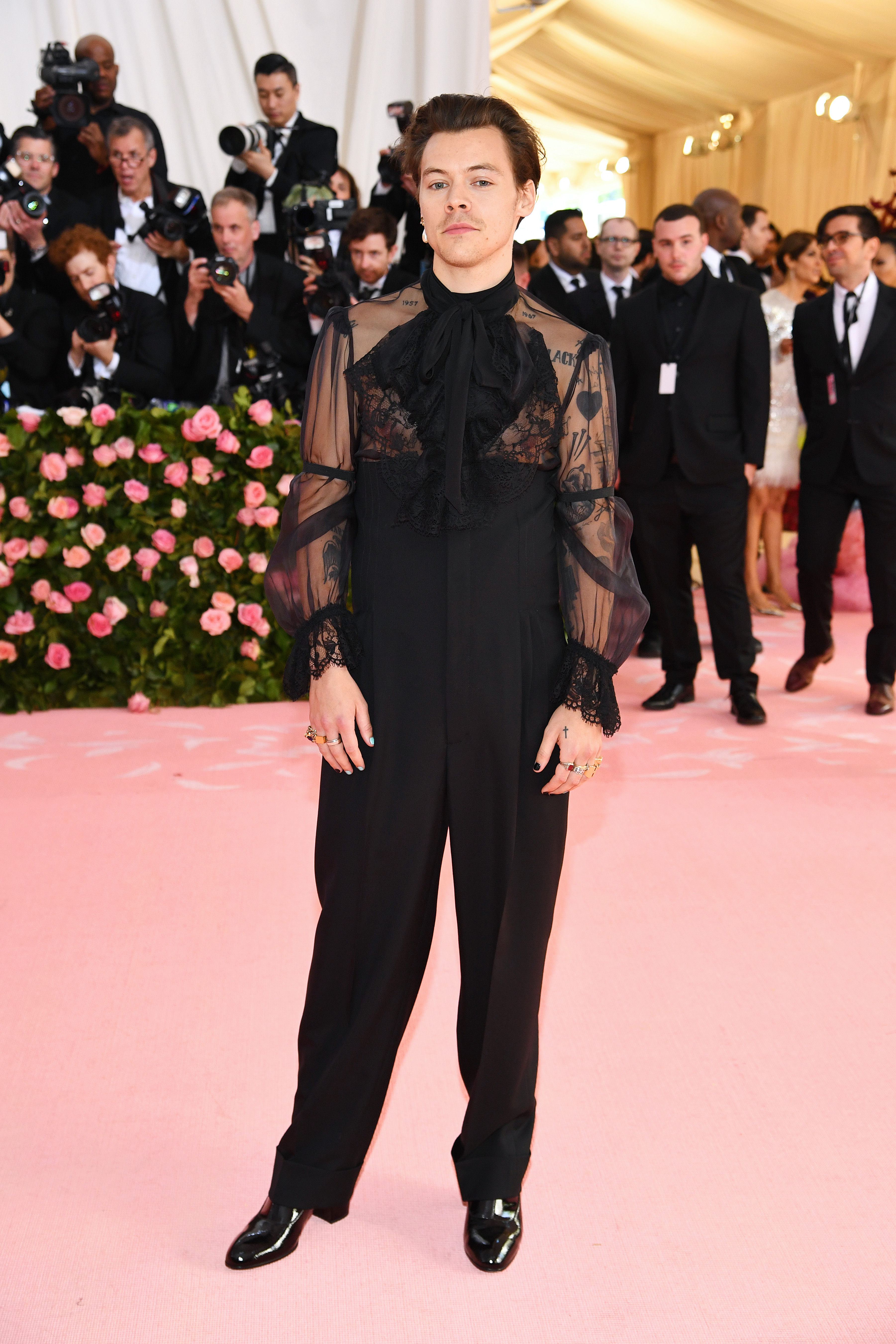 Harry Styles no MET Gala 2019 usando look todo preto com macacão que possui a parte de cima transparente