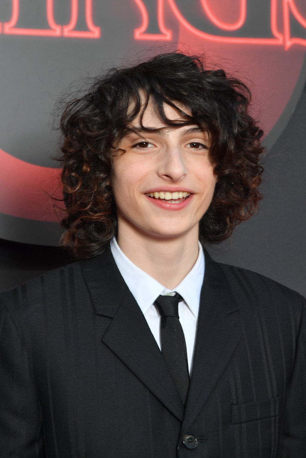 Finn Wolfhard na premiere da 3ª temporada de Stranger Things em Paris; ele está sorrindo e usando um terno enquanto posa para foto