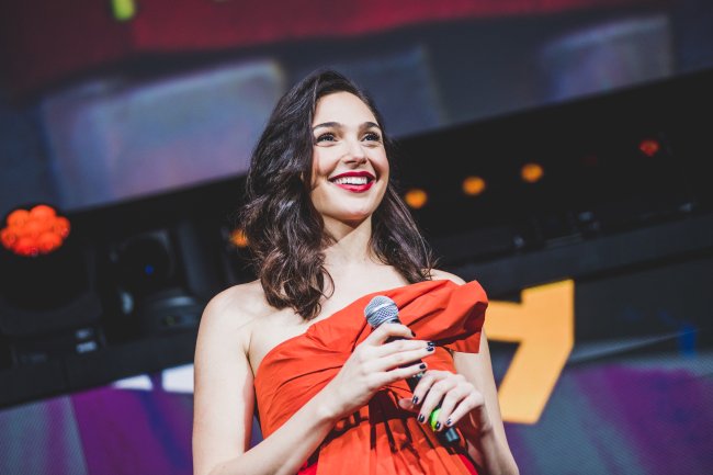 Gal Gadot segurando microfone enquanto olha para o público em painel da CCXP19, em São Paulo, com roupa vermelha e cabelo solto