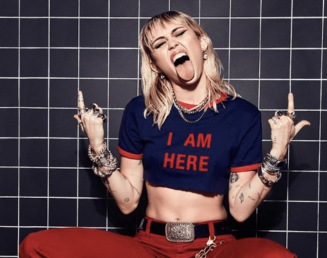 Miley Cyrus mostrando a língua e apontando para cima