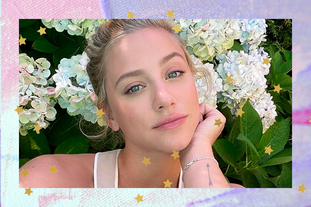 Lili Reinhart na frente de algumas flores posando com a mão esquerda sob o quixo