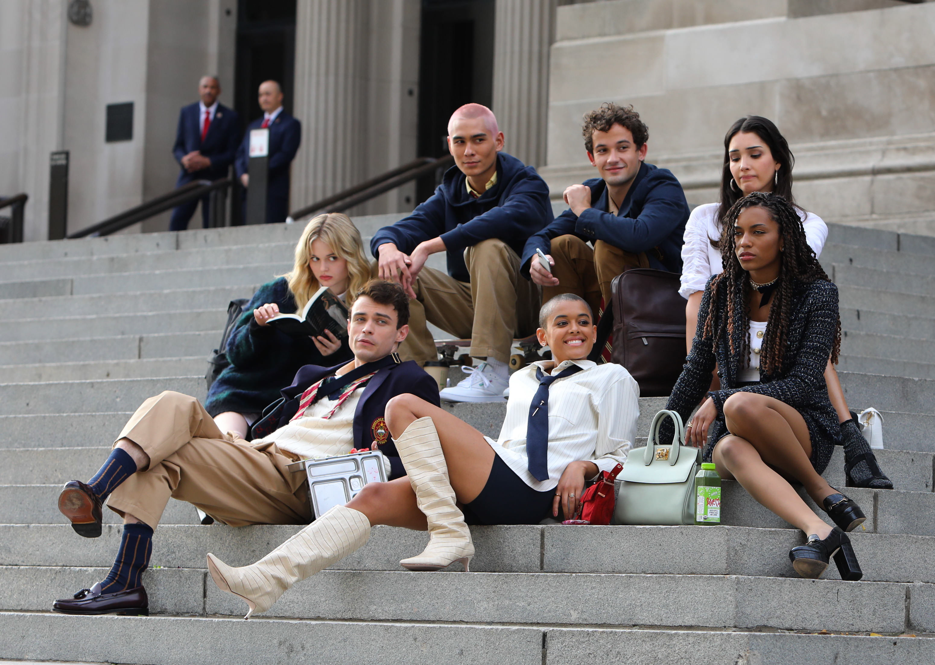 Elenco do reboot de Gossip Girl sentado na escadaria do MET, em Nova Iorque. Alguns atores estão olhando para tela ou sorrindo enquanto outros estão com expressões sérias