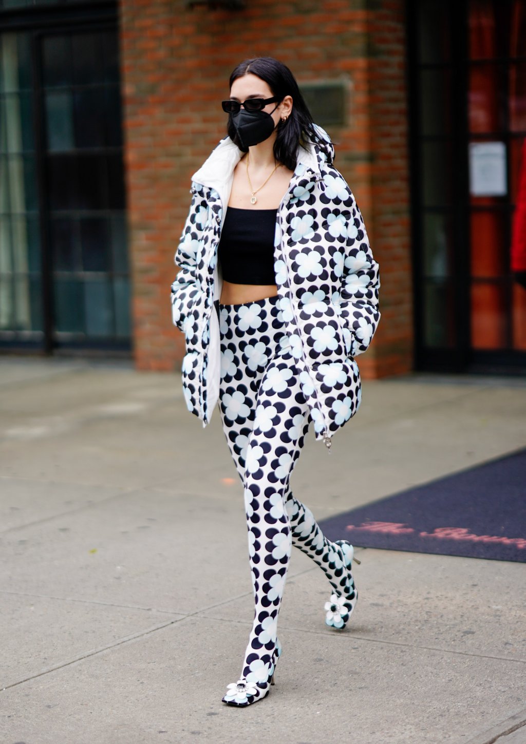 Dua Lipa usando look todo de estampa floral com casaco puffer, regatinha preta básica, legging e sapato de salto