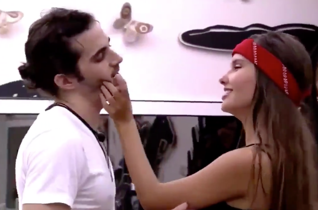 Fiuk e Thaís no BBB21. Eles estão de lado para a câmera e ela está sorrindo, com a mão no rosto dele