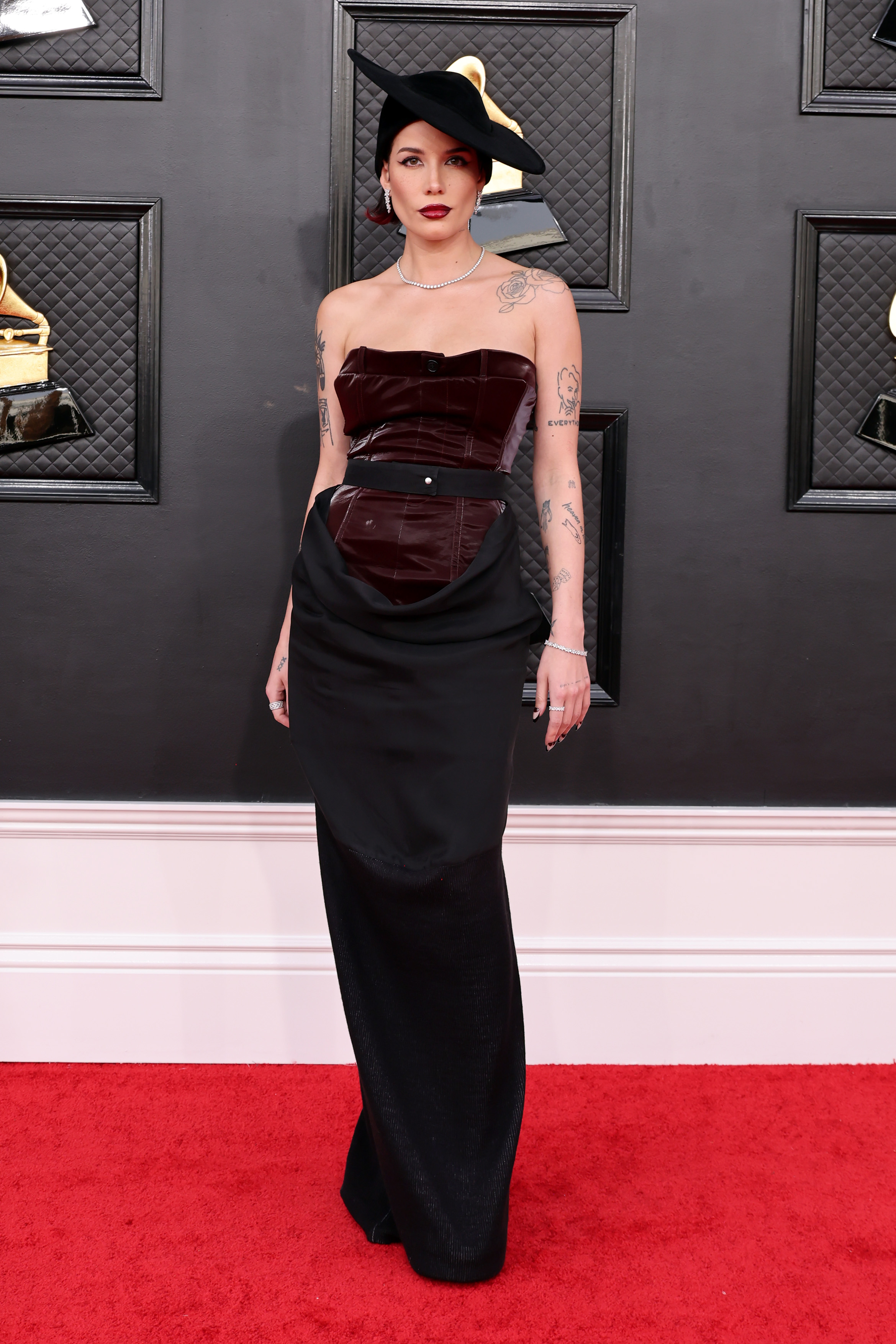 64th Annual GRAMMY Awards – Arrivals Imagem mostra Halsey no tapete vermelho da 64ª edição do Grammy Awards usando um vestido tomara que caia marrom e preto Pressiat, acompanhado de chapéu Pierra Cardin dramático, inclinado e de aba larga.
