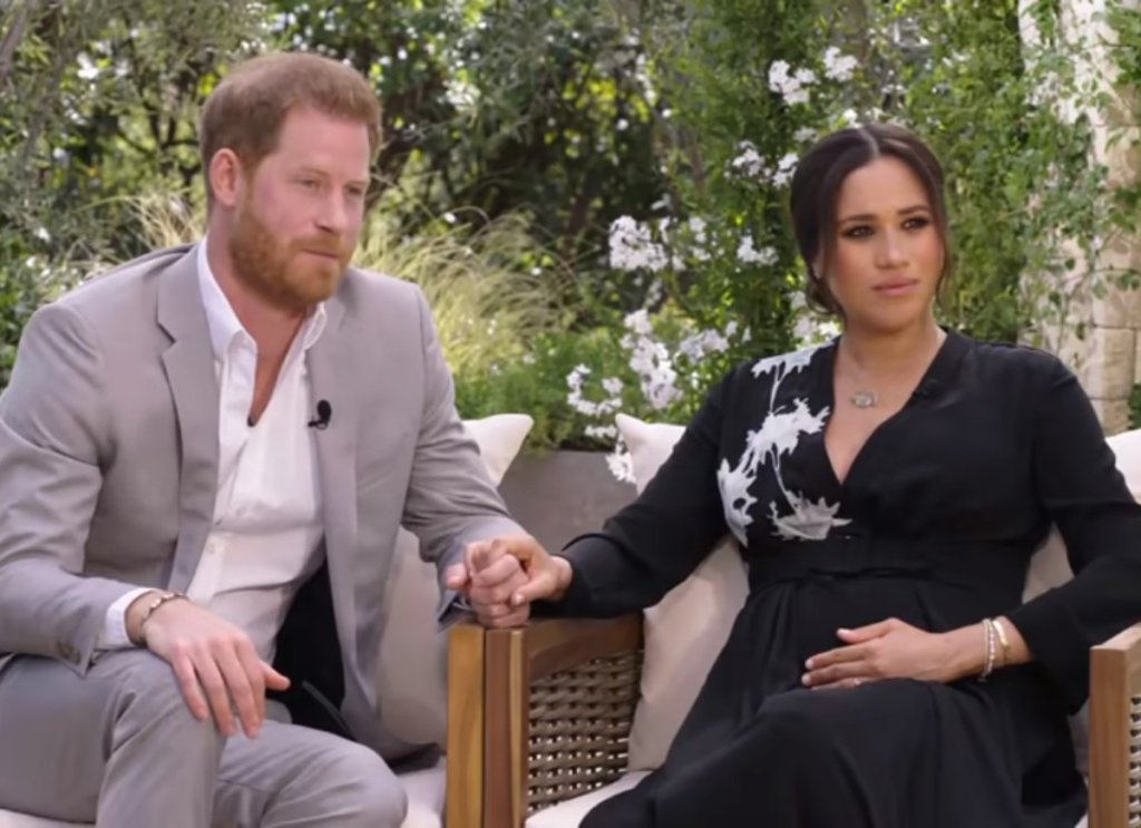 Príncipe Harry e Meghan Markle sentados e de mãos dadas