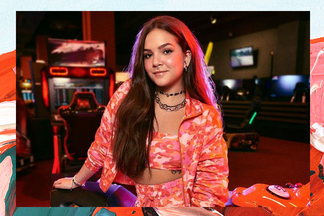 Mel Maia usando conjuntinho laranja e sorrindo levemente para a câmera