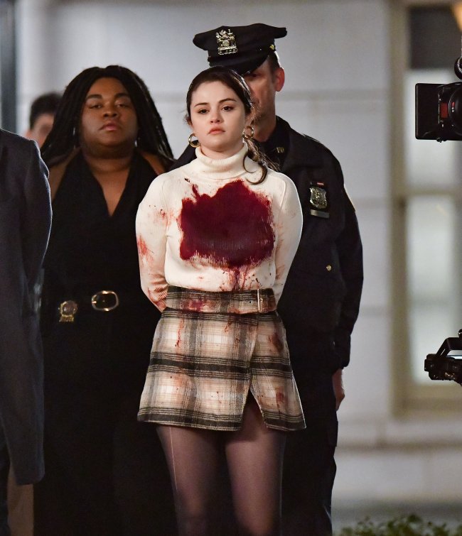 Celebrity Sightings In New York City – April 10, 2021 Selena Gomez aparece com uma macha de sangue em seu sueter bege de bola alta, sendo escoltada pela polícia, com as mãos para trás no set de filmagens da série