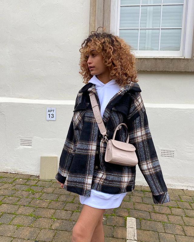 tendencia-outono-inverno-sofiaelhaj Garota usando casaco xadrez por cima de blusa de moletom oversized branca e uma bolsa atravessada bege. Ela está olhando para o lado e a foto só pega até a a altura da coxa.