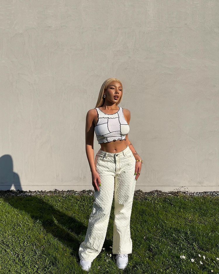 tendencia-patchwork-goldslumberkisses Garota usando blusa cropped branca de patchwork com calça baggy amarela-clara e tênis branco. Ela está em pé, com as duas mãos apoiadas na perna, expressão séria olhando para o lado.