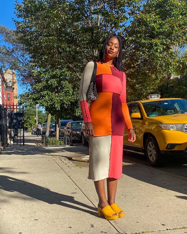 tendencia-patchwork-thelanguageofyolande Garota usando vestido midi de manga longa de patchwork nas cores laranja, bordô, vermelho e bege. Ela está com um tamanco amarelo e uma bolsa de estampa de zebrinha pendurada em um dos ombros. Ela está em pé, olhando em direção à câmera, que tira a foto de cima para baixo.
