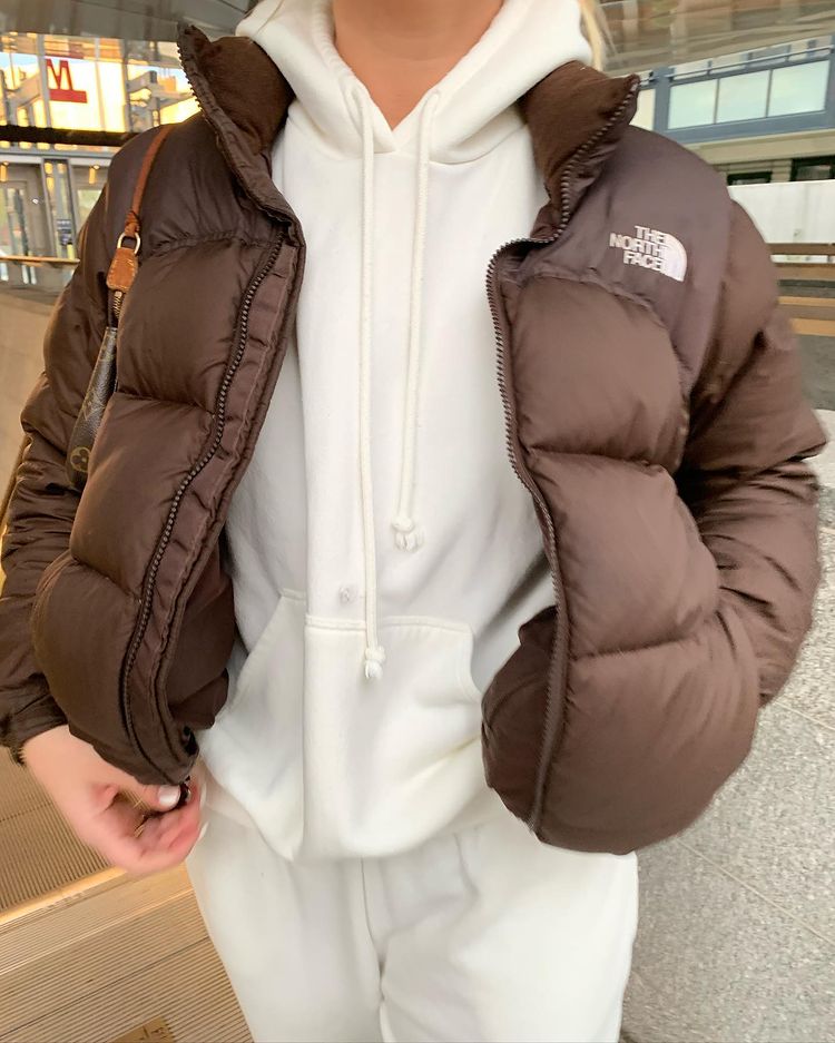 tendencias-outono-inverno-barbarakristoffersen-02 Mulher usando conjunto de moletom off-white com jaqueta puffer marrom por cima. A foto só dá para ver do pescoço pra baixo e pega um pouco da calça. Uma das mãos está no bolso.