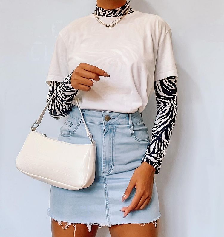 Garota usa blusa segunda pele por baixo de camiseta bege básica, com saia jeans clara e bolsa baguete off-white pendurada em um dos braços. A foto mostra apenas do pescoço para baixo até a altura da coxa.