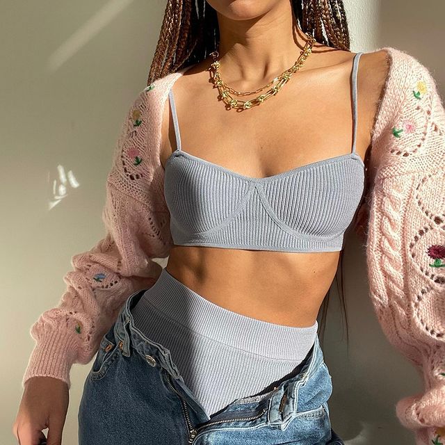 top-cropped-sutia-amaka.hamelijnck Garota usando top cropped azul pastel com hot pants da mesma cor. Ela está com uma calça jeans por cima desabotoada, além de um cardigan de tricô rosa com furinhos e flores bordadas e um colar de correntes douradas. Na foto, dá apenas para ver do pescoço para baixo até a altura do quadril.