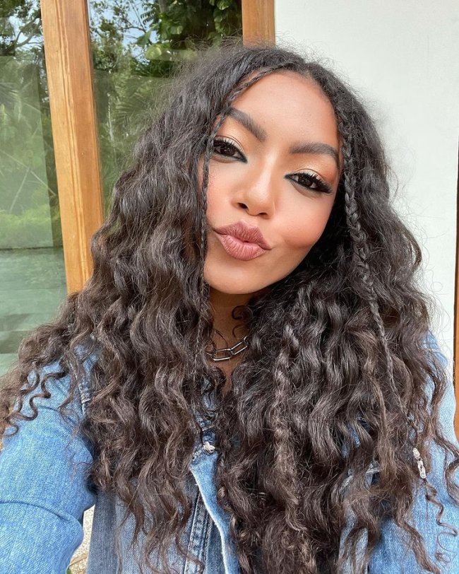 Any Gabrielly, representante brasileira do Now United, aprece posando para fotos, fazendo biquinho e com trancinhas finas nas mechas da frente de seu cabelo.