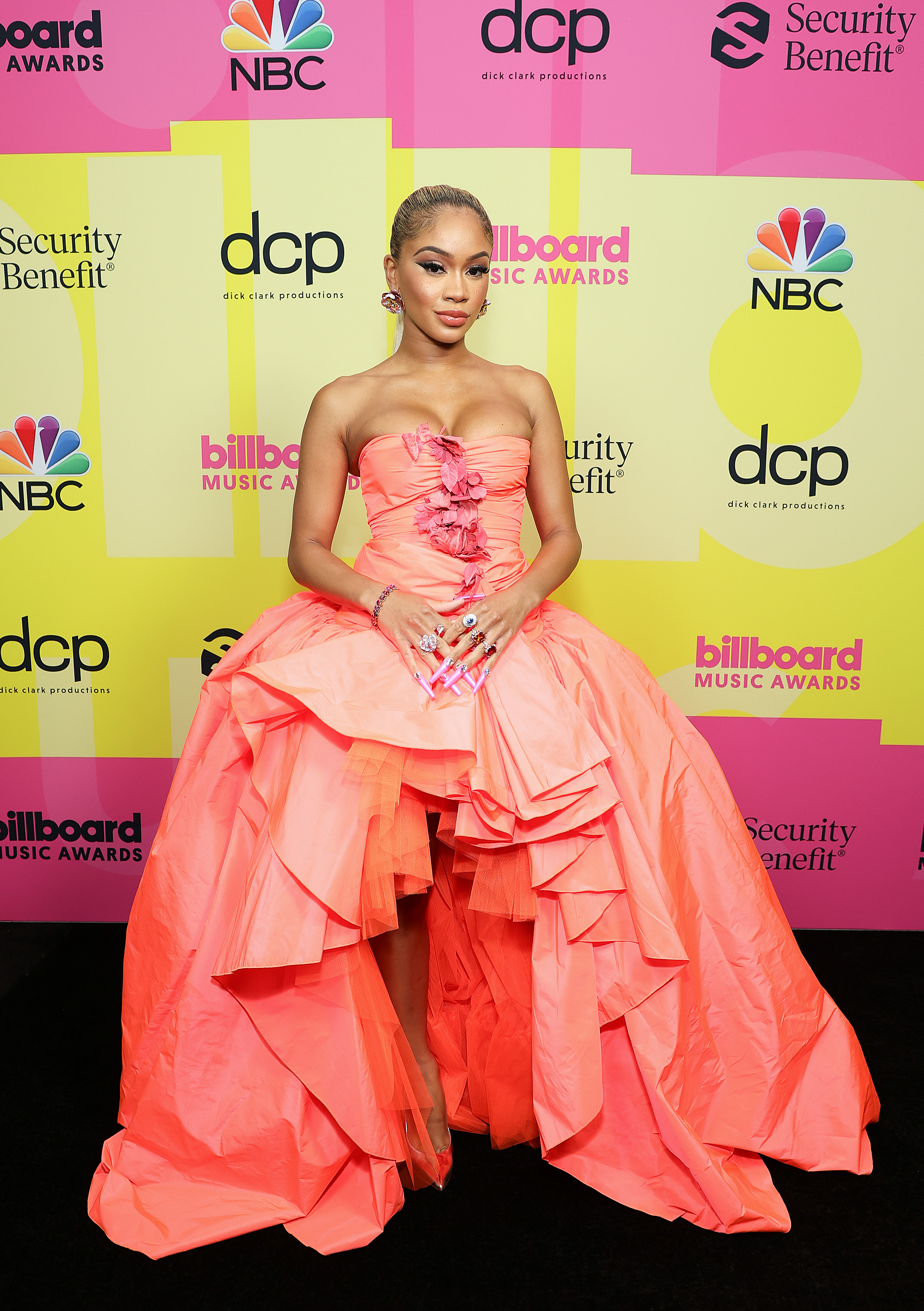 Saweetie no Billboard Music Awards 2021. Ela está usando um vestido laranja sem alças com saia volumosa e abertura na parte da frente.