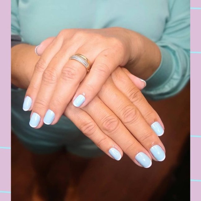 Foto mostrando uma mão com os dedos dobrados para evidenciar as unhas pintadas em francesinha colorida nas cores azul e branco.