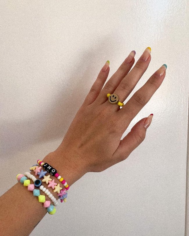 Foto mostrando uma mão com os dedos dobrados para evidenciar as unhas pintadas em francesinha colorida nas cores cinza, laranja, lilas, amarelo e vermelho.