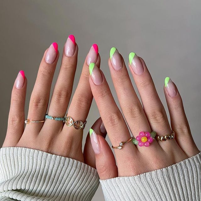 Foto mostrando uma mão com os dedos dobrados para evidenciar as unhas pintadas em francesinha colorida sendo uma das mãos com a unha rosa e a outra verde.