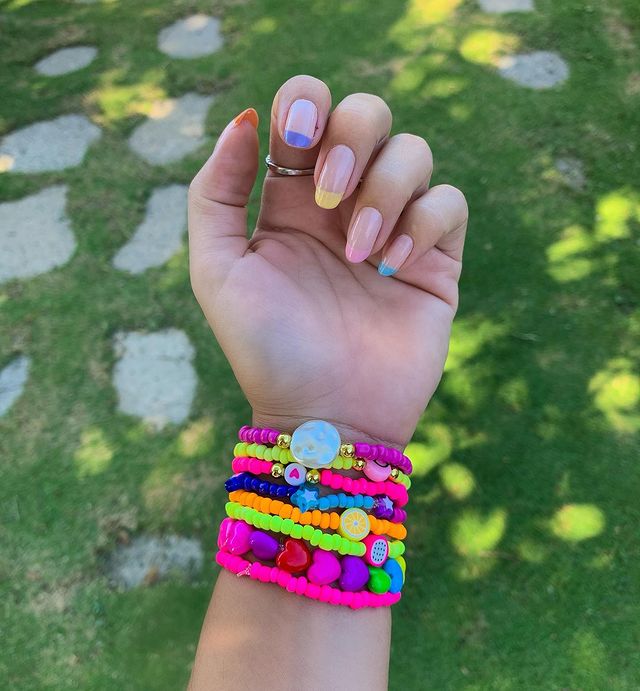 Foto mostrando uma mão com os dedos dobrados para evidenciar as unhas pintadas em francesinha colorida nas cores amarela, rosa, azul, lilas e laranja.