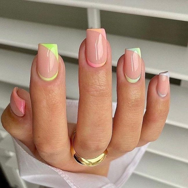 Foto mostrando uma mão com os dedos dobrados para evidenciar as unhas pintadas em francesinha colorida nas cores verde, laranja e lilas.