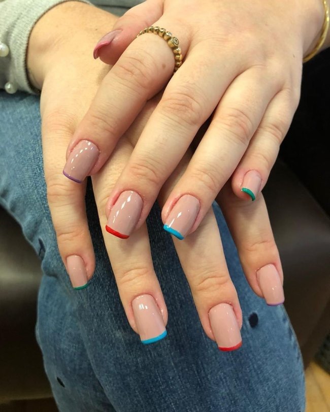 Foto mostrando uma mão com os dedos dobrados para evidenciar as unhas pintadas em francesinha colorida nas cores cinza, laranja, lilas, amarelo e vermelho.