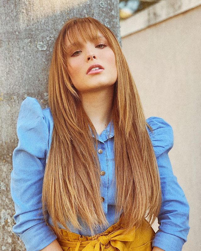 Larissa Manoela com expressão séria, posando para foto com a cabeça levemente levantada com camisa jeans com manga bufante.