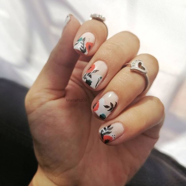 Dedos dobrados com anel exibindo nail art com base clara e detalhes laranja e preto.