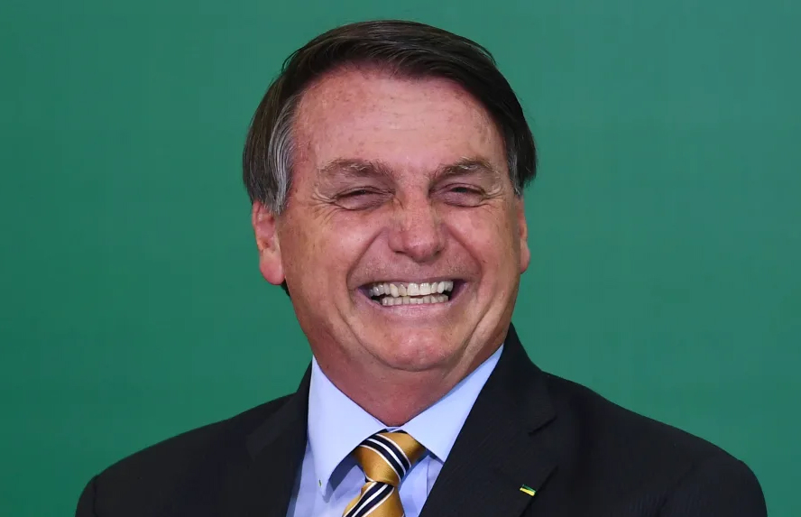 Jair Bolsonaro rindo bastante; ele está sobre um fundo verde