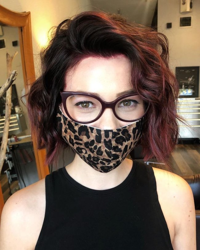 cabelo curto ruivo Jovem com cabelo curto e levemente vermelho, com máscara de proteção com estampa de oncinha, usando regata preta.