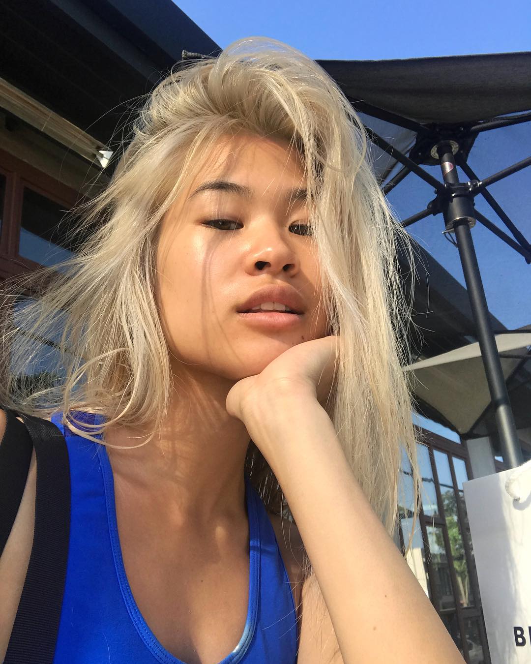 cabelo_loiro Selfie de uma mulher. Ela usa uma regata azul e está com o cabelo loiro solto. Ela apoia o rosto na mão esquerda, olha para a câmera e não sorri para a foto.