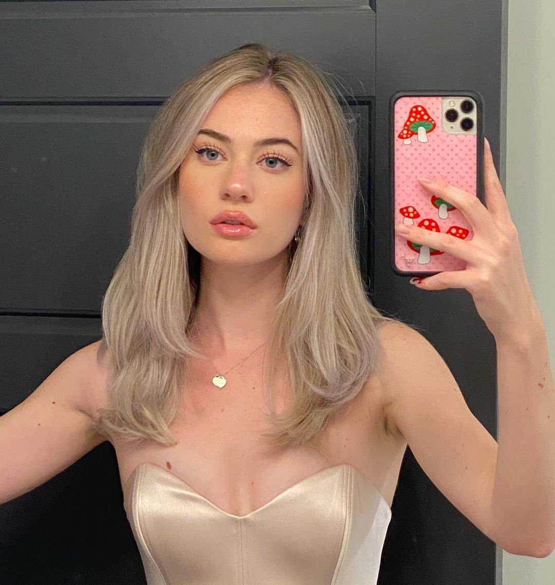 cabelo_loiro_perolado Selfie no espelho de uma mulher. Ela usa um top corset nude e está com o cabelo solto. Ela olha para o espelho e não sorri.