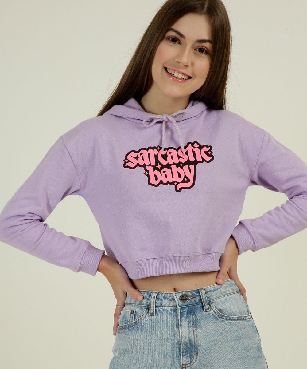 colecao-capricho-marisa-06 Garota usando blusa de moletom lilás escrito sarcastic baby da coleção da CAPRICHO com a MARISA. Ela está sorrindo, com as duas mãos apoiadas na cintura e também dá para ver um pedaço da calça jeans.