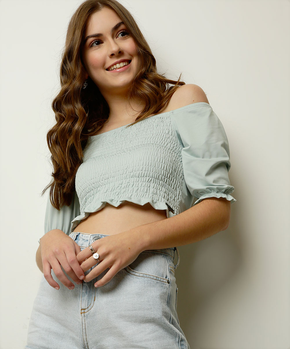 colecao-capricho-marisa-10 Garota usando top verde e short jeans da coleção da CAPRICHO com a MARISA. Ela está sorrindo, olhando para o lado e com as duas mãos na frente do corpo.