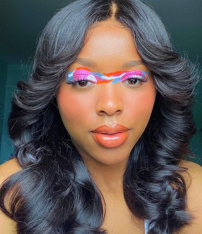 delineado unificado colorido Foto com close no rosto da jovem com expressão seria, ela usa delineado unificado nas cores azul, branco, laranja e rosa.