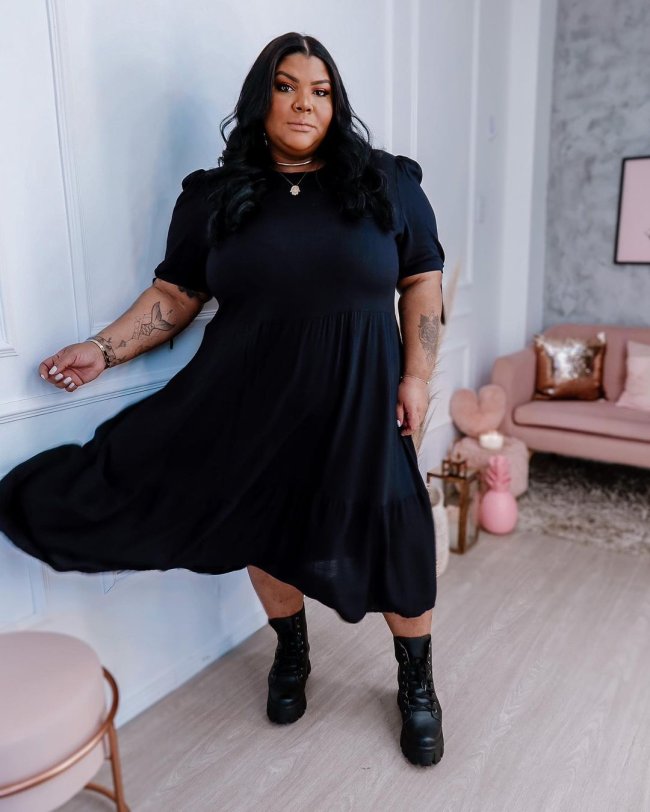 look com coturno preto Jovem posando com lado do vestido levemente no ar, com expressão séria e os braços ao lado do corpo, usando vestido e coturno preto.