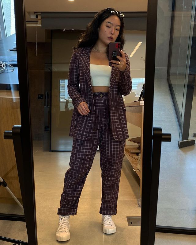 look xadrez Selfie no espelho de uma mulher. Ela usa um blazer xadrez, cropped branco, calça xadrez e tênis branco. Ela não sorri para a foto.