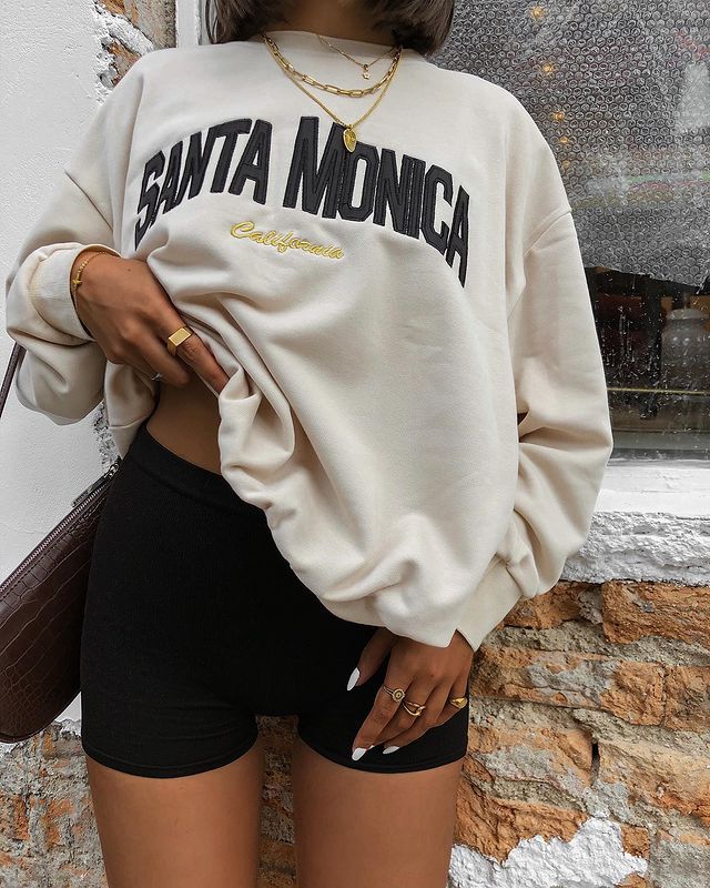 look_moletom_vintage_biker_shorts Foto apenas do look de uma mulher. Ela veste um biker shorts preto, moletom vintage bege e bolsa baguete na cor marrom.