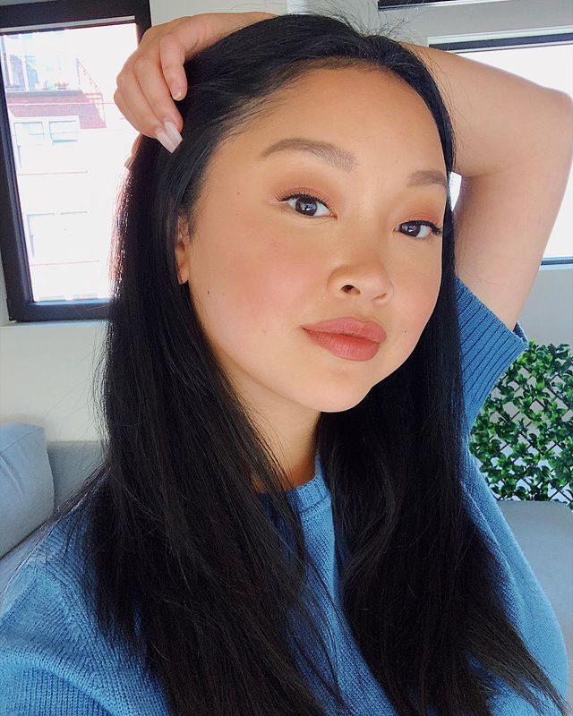 Selfie da atriz Lana Condor. Ela usa uma camiseta azul, cabelo solto, make natural com batom nude. Ela olha para a câmera, segura a cabeça com a mão esquerda e sorri para a foto.