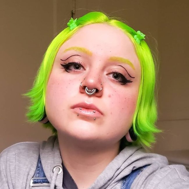 presilha de borboleta verde Jovem com expressão séria com cabelo verde, e a cabeça levemente inclinada para cima.