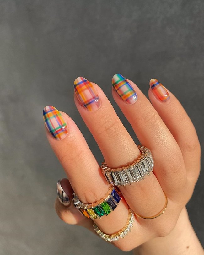 unhas coloridas xadrez Foto de uma mão com anéis no dedo indicador e médio. A unha está com uma nail art xadrez colorida.