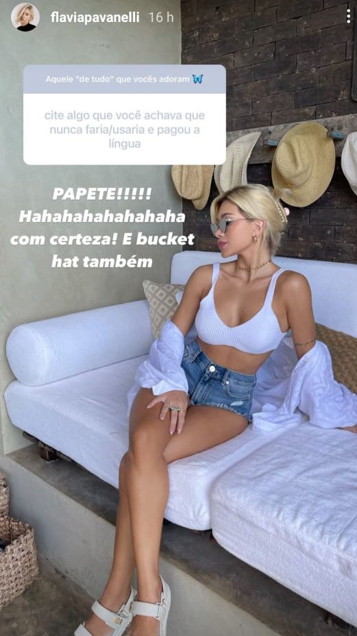 Flavia Pavanelli Print do instagram de Flavia Pavanelli posando em uma foto sentada em um sofá branca, top, camiseta, short, usando coque e sentada virada para o lado direito.