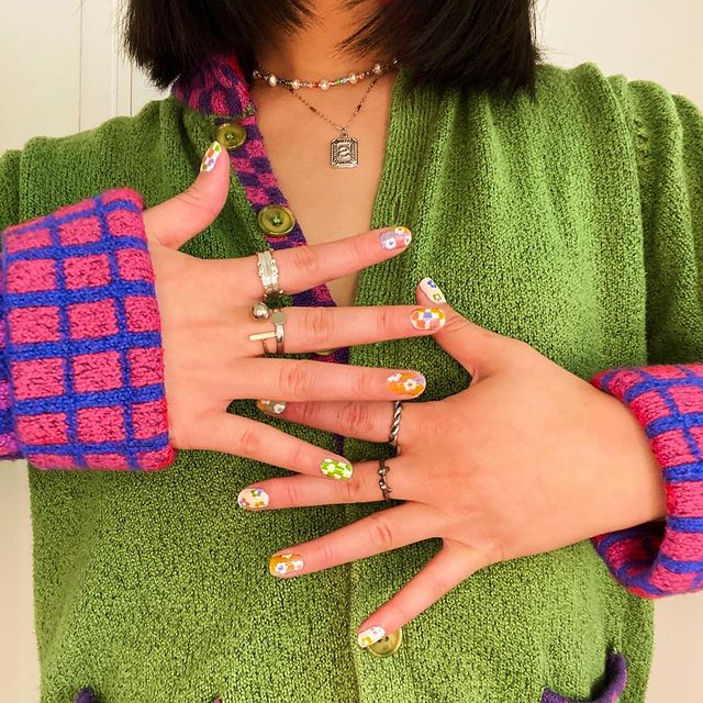 acessórios avant basic Foto do colo de uma mulher usando diversos anéis e colares com um cardigan verde com manga estampada.