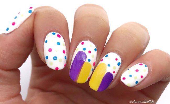 Foto com destaque nas unhas com nail art de bolinha, dessa vez com fundo branco e bolinhas nas cores azul e vermelho e detalhes em roxo e amarelo.