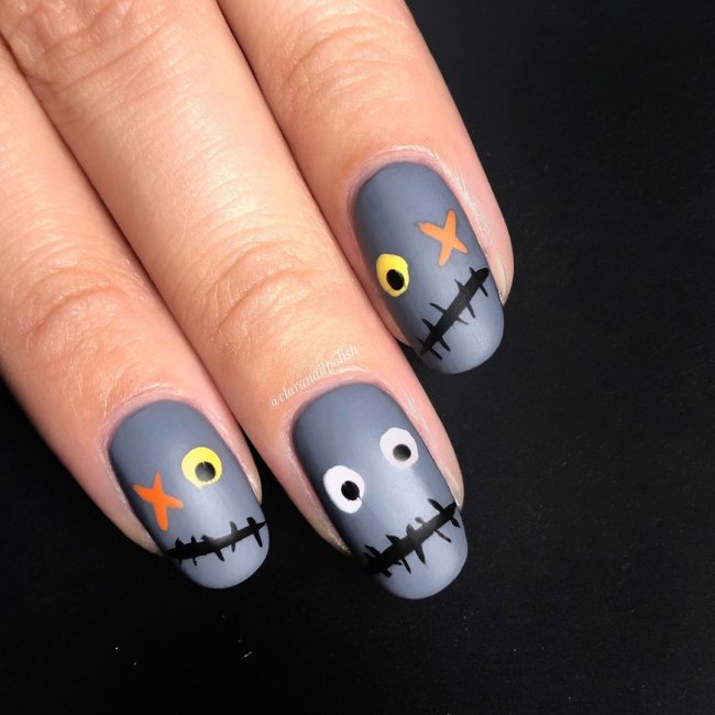 Foto com destaque nas unhas com nail art de bolinha, dessa vez com fundo cinza e formando um monstrinho com olhos de bolinha nas cores cinza, preto, laranja e amarelo.