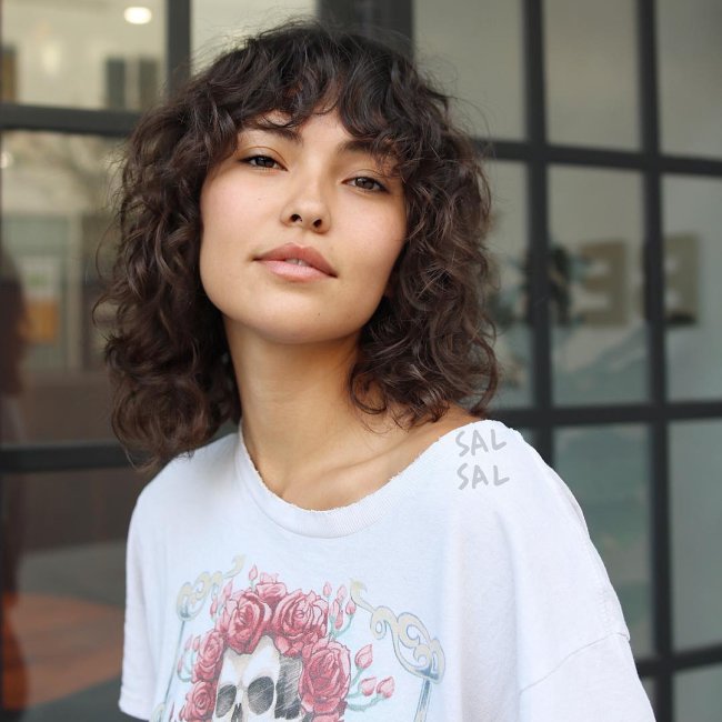 Jovem com a cabeça levemente inclinada, usando camiseta com estampa de coroa. Sua expressão é sorridente.