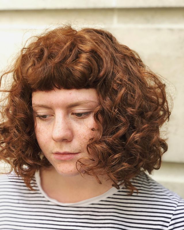 franja cabelo cacheado Jovem com expressão levemente sorridente, exibindo seu corte bob, usando blusa branca com listras
