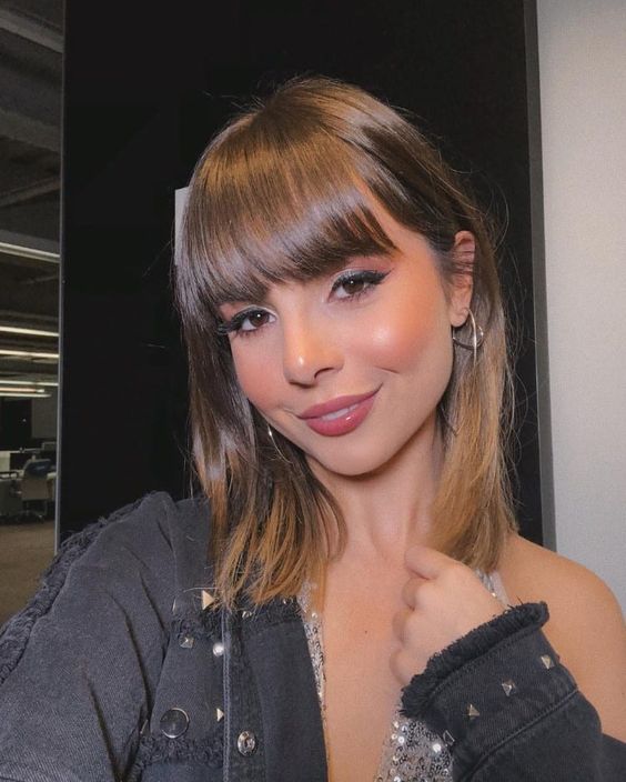 franja reta Selfie da blogueira Giovanna Ferrarezi. Ela usa uma jaqueta preta, cabelo solto e franja reta. Ela olha para a câmera e sorri.